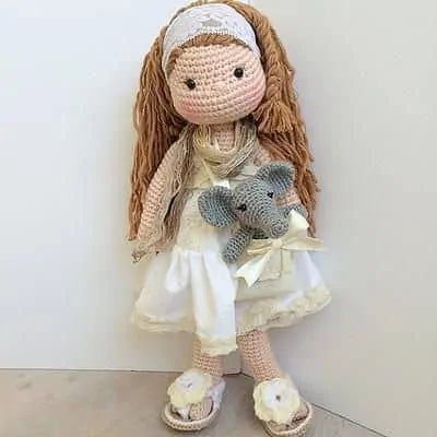 Crochet doll with light brown hair, yellow and white fabric dress and crochet tiny elephant