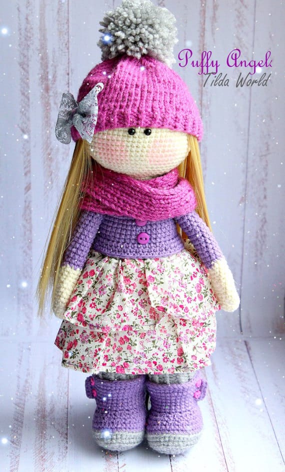 Crochet doll with pink hat, blond hair, pink and purple outfit with fabric skirt