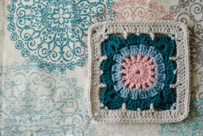 crochet afghan square on fabric in ivory, blue, pink and gray