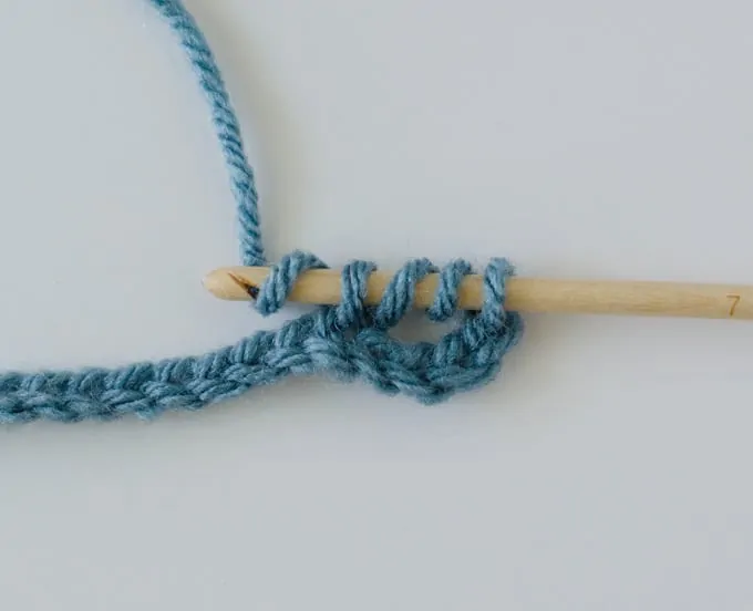 Crochet treble stitch in progress with blue yarn and wood hook