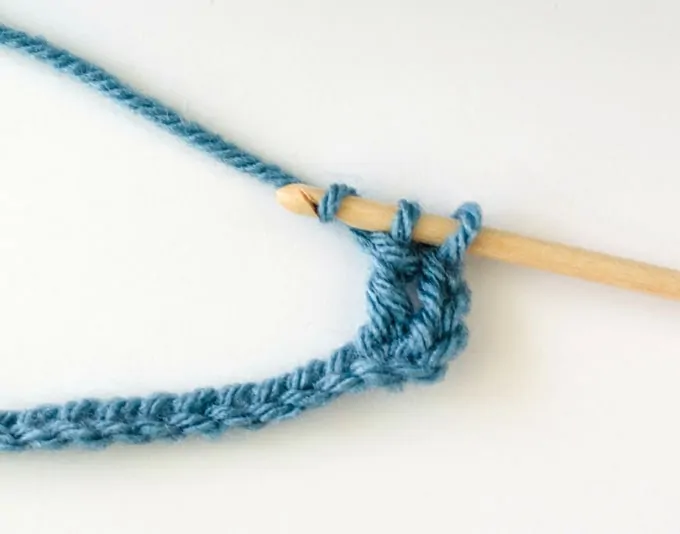 Crochet treble stitch in progress with blue yarn and wood hook