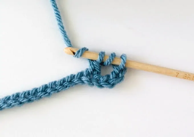 Crochet treble stitch in progress with blue yarn and wood hook