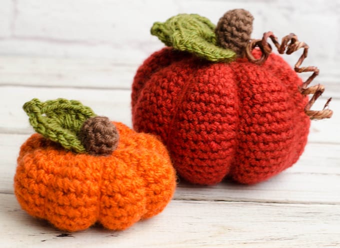small orange crochet pumpkin and medium darker crochet pumpkin with green leaves and brown stems