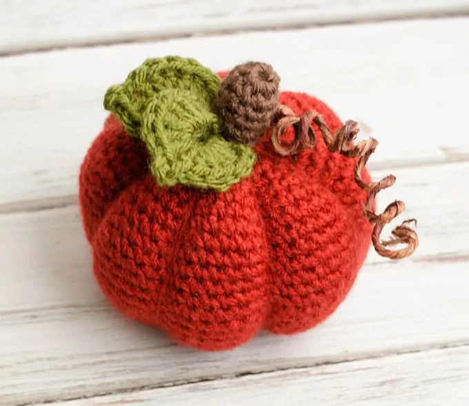 orange crochet pumpkin with green leaf, brown stem and curly tendril