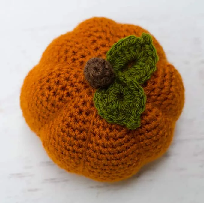 top view of orange crochet pumpkin featuring two green leaves and brown stem