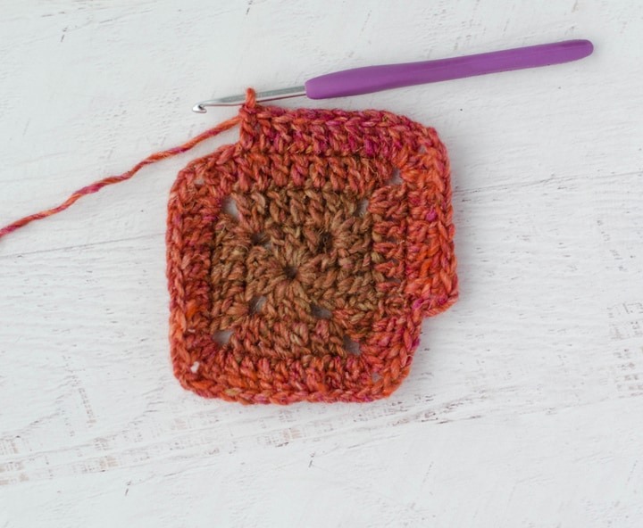 Solid Granny Square in progress with multi color red yarn and purple crochet hook