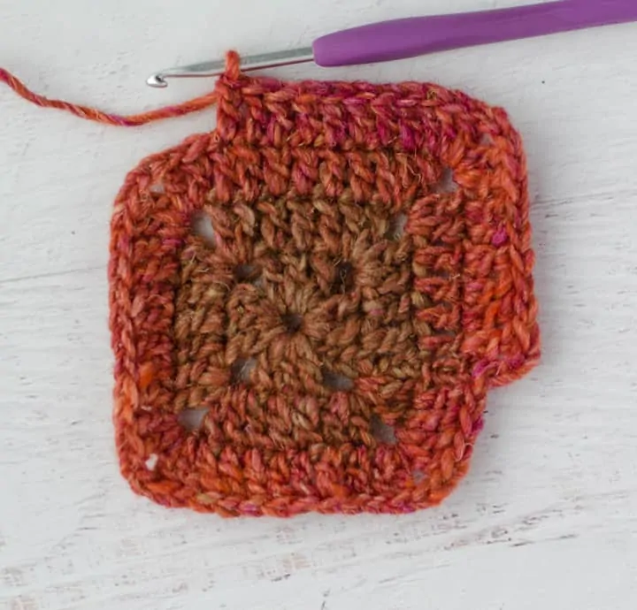 Solid Granny Square in progress with multi color red yarn and purple crochet hook