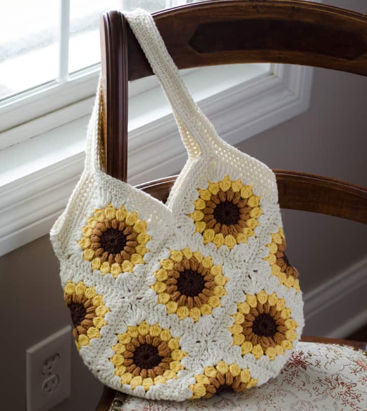 crochet granny square bag in off-white, yellow, gold and brown yarn on chair