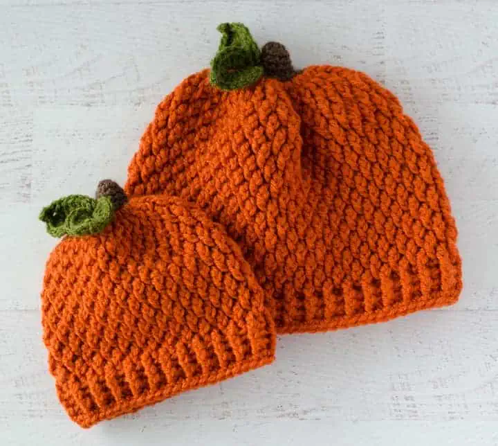 Two orange crochet pumpkin hats with brown stems and green leaves