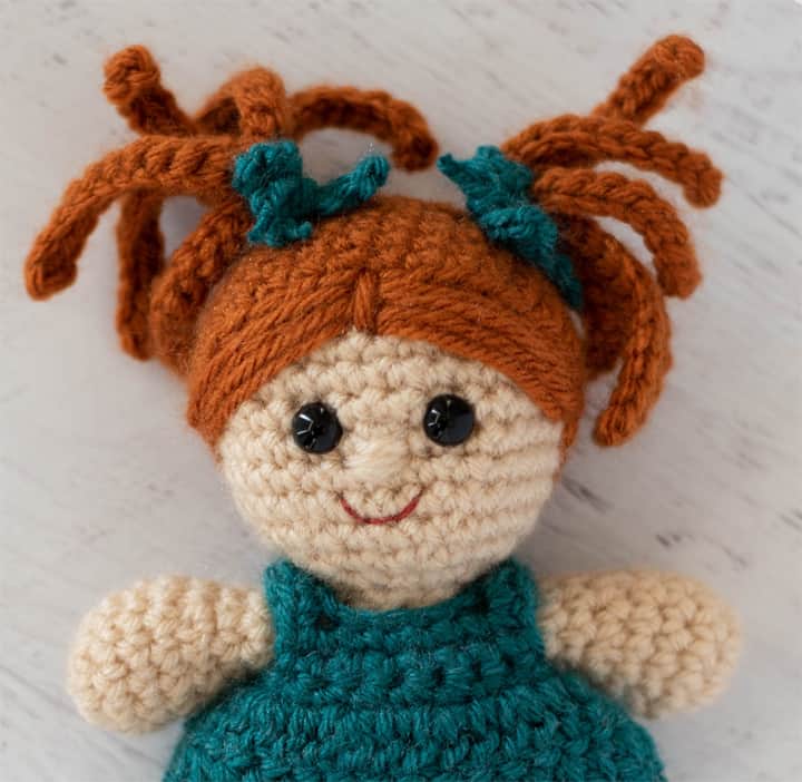 Crochet doll head with rust color hair, eyes and smile