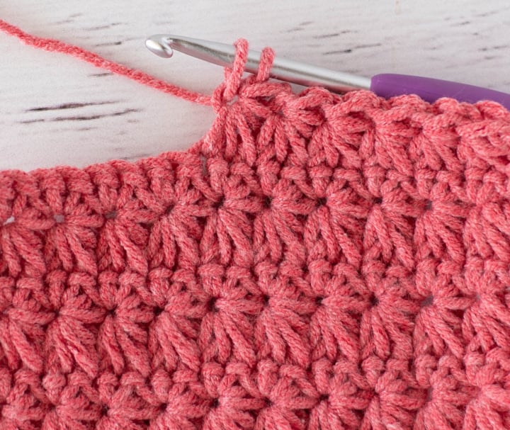 Close up view of how to make a crochet star stitch with coral colored yarn