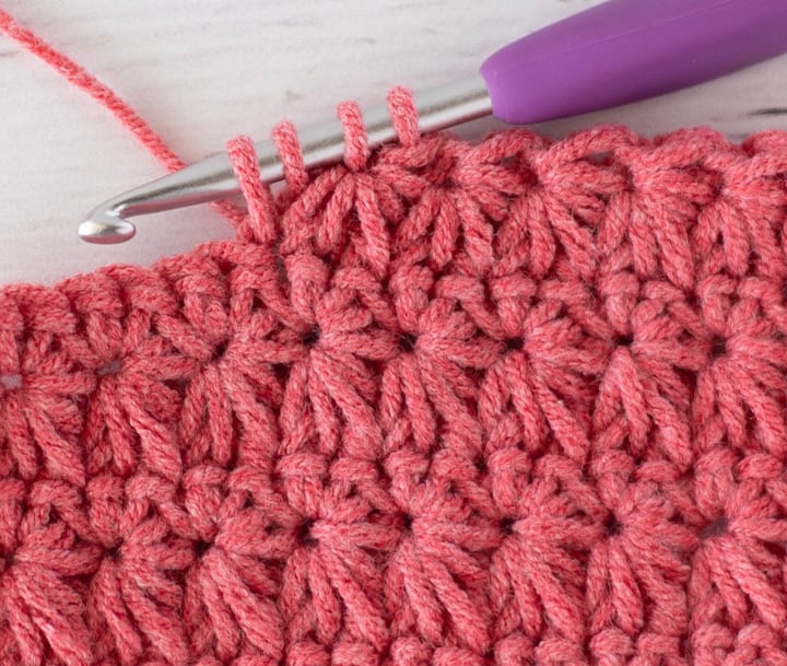 Close up view of how to make a crochet star stitch with coral colored yarn