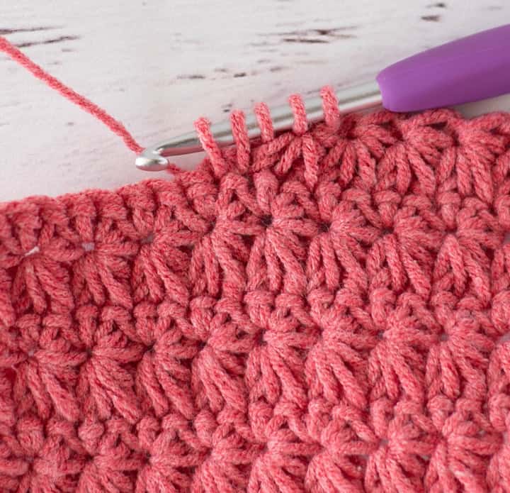 Close up view of how to make a crochet star stitch with coral colored yarn
