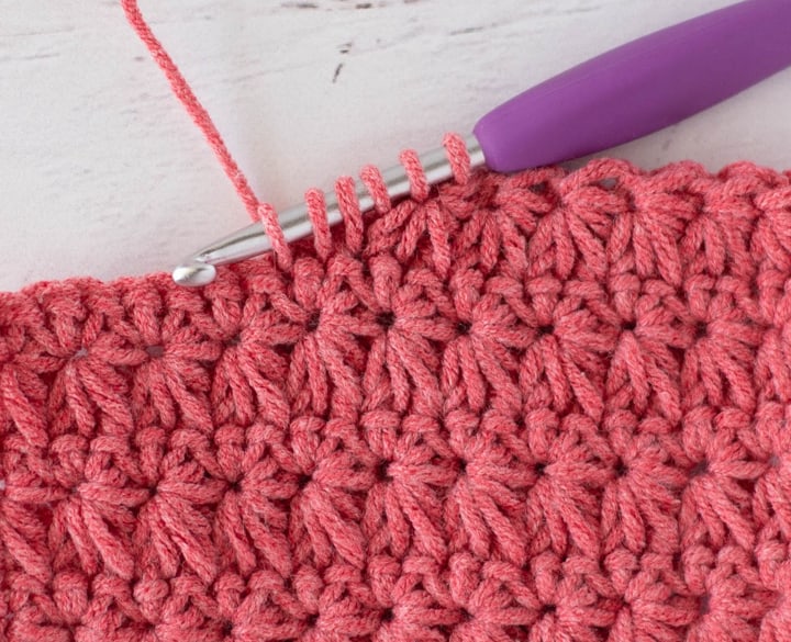 Close up view of how to make a crochet star stitch with coral colored yarn