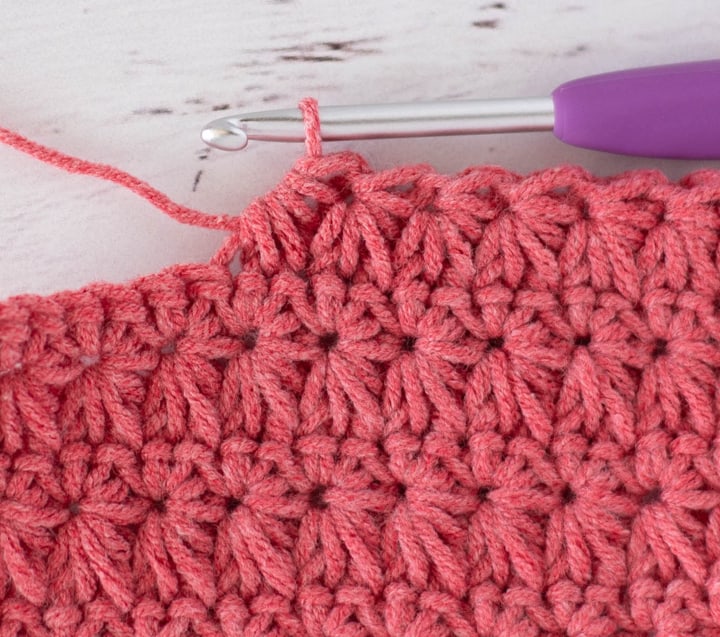 Close up view of how to make a crochet star stitch with coral colored yarn