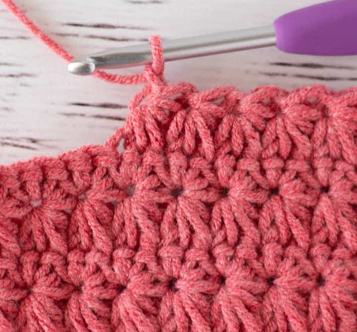 Close up view of how to make a crochet star stitch with pink yarn
