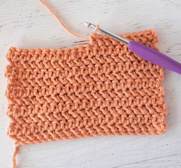 salmon color yarn swatch of herringbone stitch with crochet hook