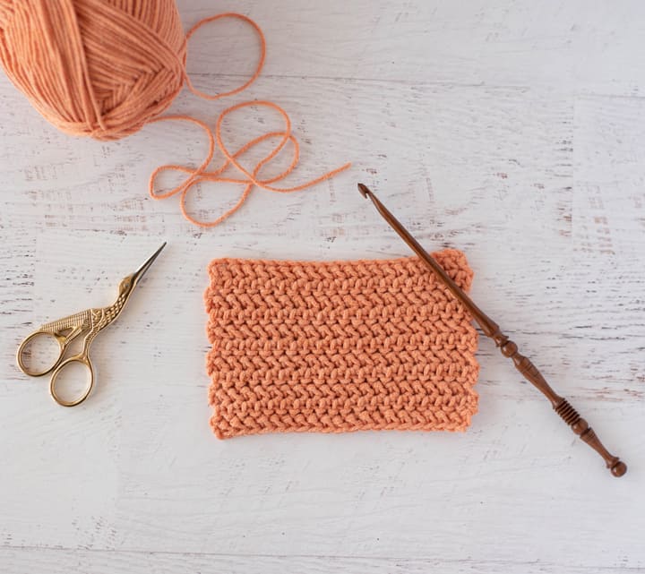 Herringbone half double crochet stitch swatch with yarn, hook and scissors