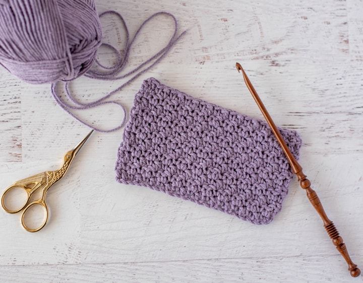 Purple crochet swatch sample of moss stitch with wooden hook and scissors