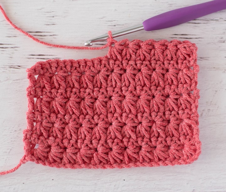 Close up view of how to make a crochet star stitch with coral colored yarn