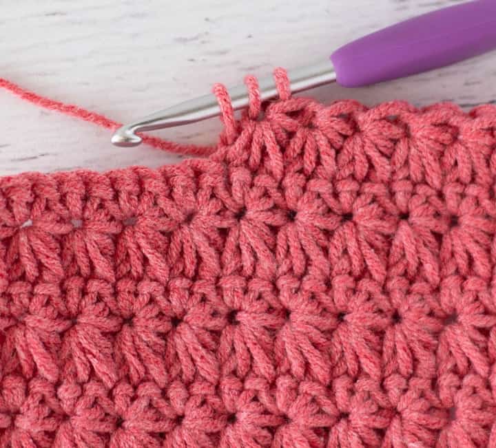 Close up view of how to make a crochet star stitch with coral colored yarn