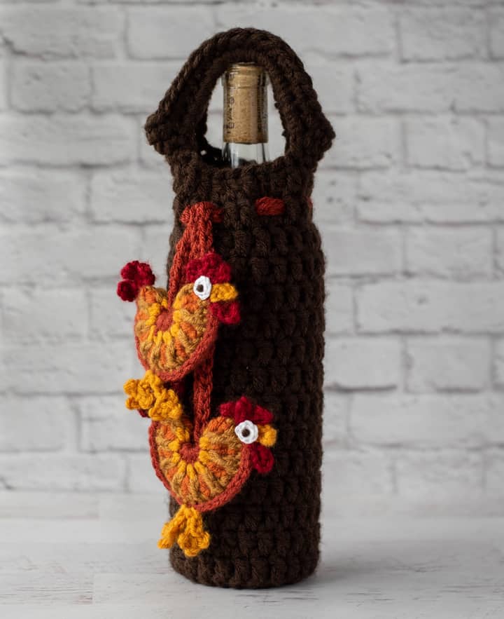 crochet rooster appliques hanging from brown wine bottle cover with bottle of wine