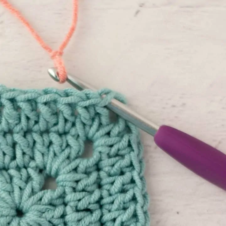 pink yarn joining two blue crochet granny squares