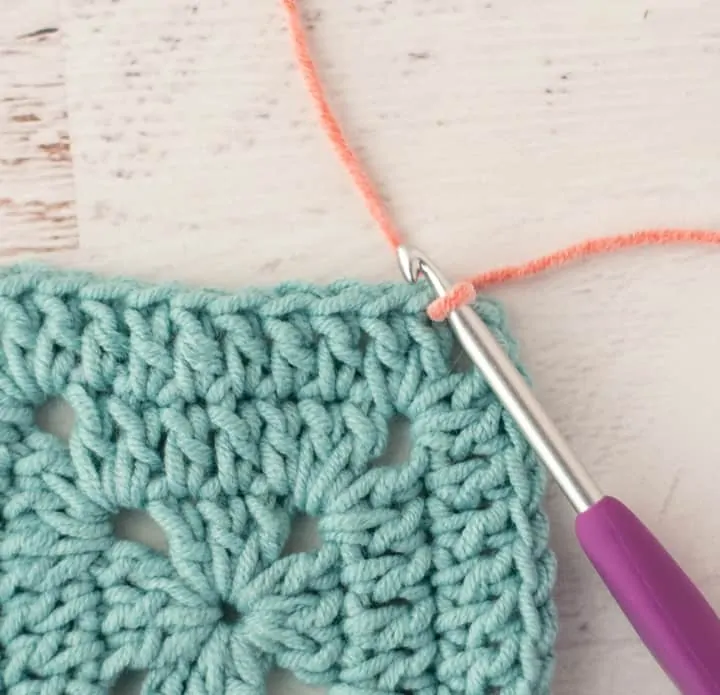 pink yarn joining two blue crochet granny squares