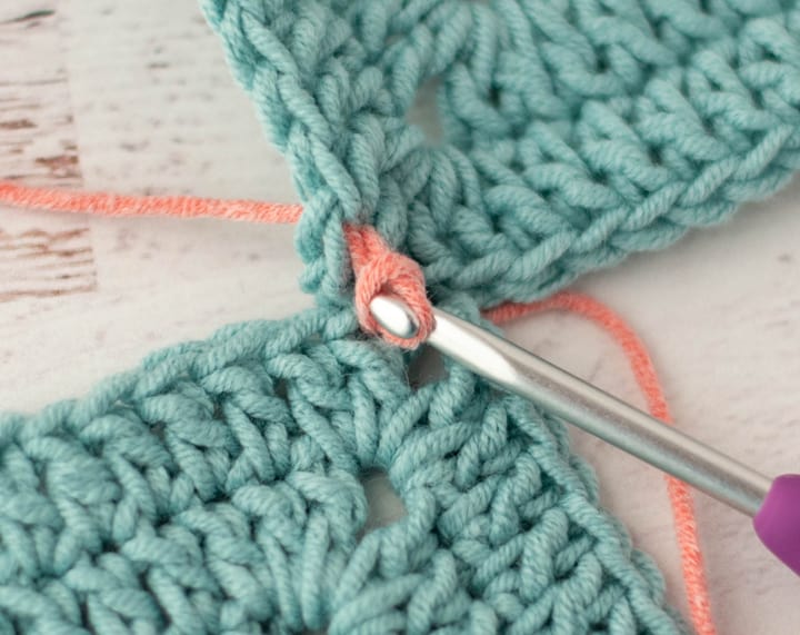 pink yarn joining two blue crochet granny squares