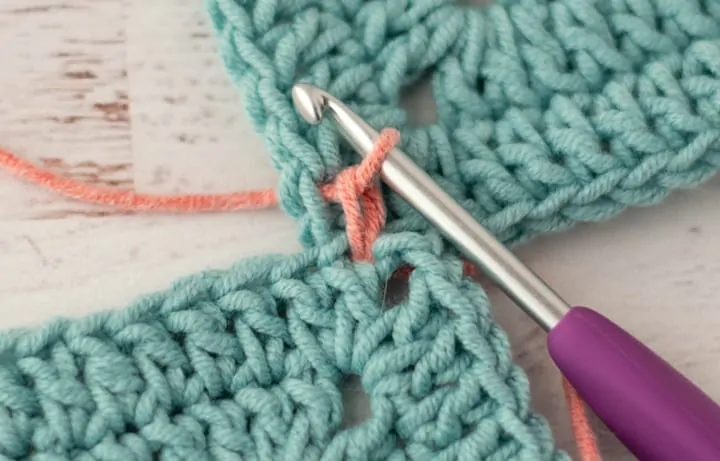 pink yarn joining two blue crochet granny squares