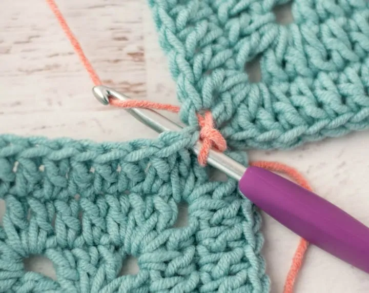 pink yarn joining two blue crochet granny squares