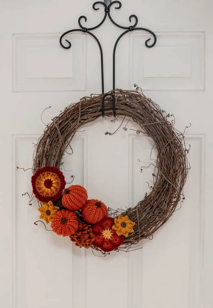 Grapevine wreath with crochet pumpkins and flowers on a white door
