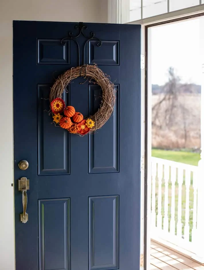 Grapevine wreath with crochet pumpkins and flowers on a blue door overlooking a porch and yard