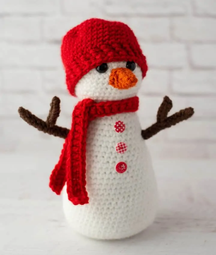 Crochet snowman with red hat and scarf, orange nose and brown twig arms