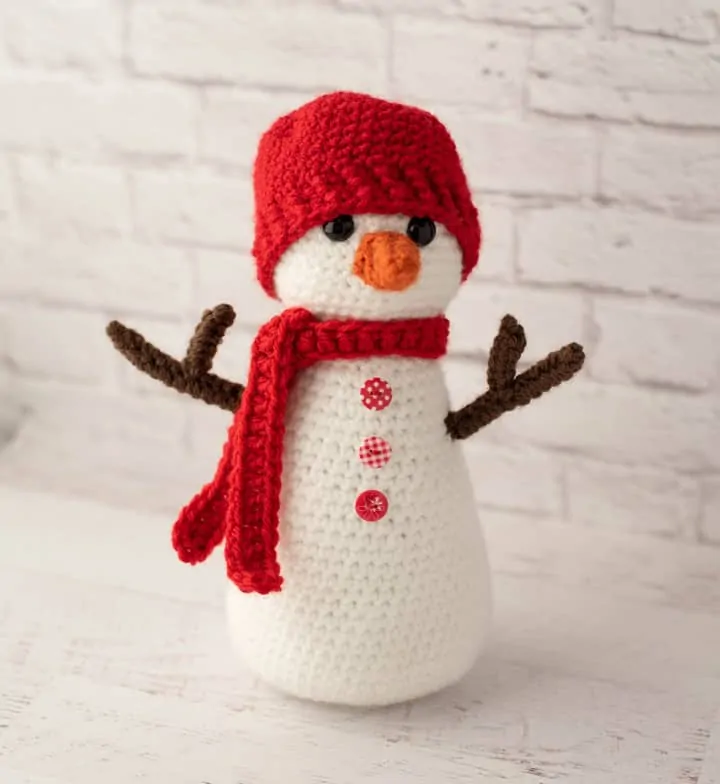 Crochet snowman with red hat and scarf, orange nose and brown twig arms