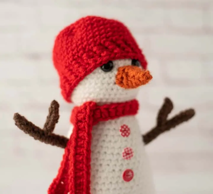 Crochet snowman with red hat and scarf, orange nose and brown twig arms