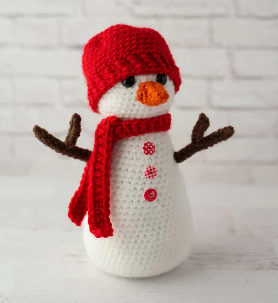 Crochet snowman with red hat and scarf, orange nose and brown twig arms