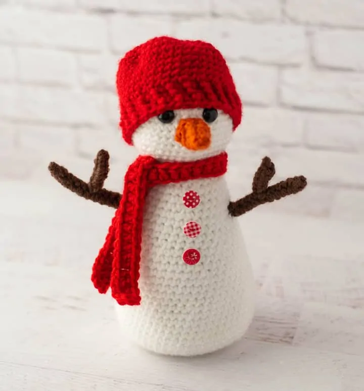 Crochet snowman with red hat and scarf, orange nose and brown twig arms