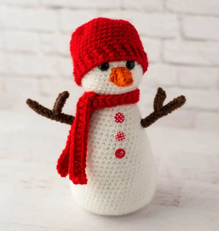 Crochet snowman with red hat and scarf, orange nose and brown twig arms