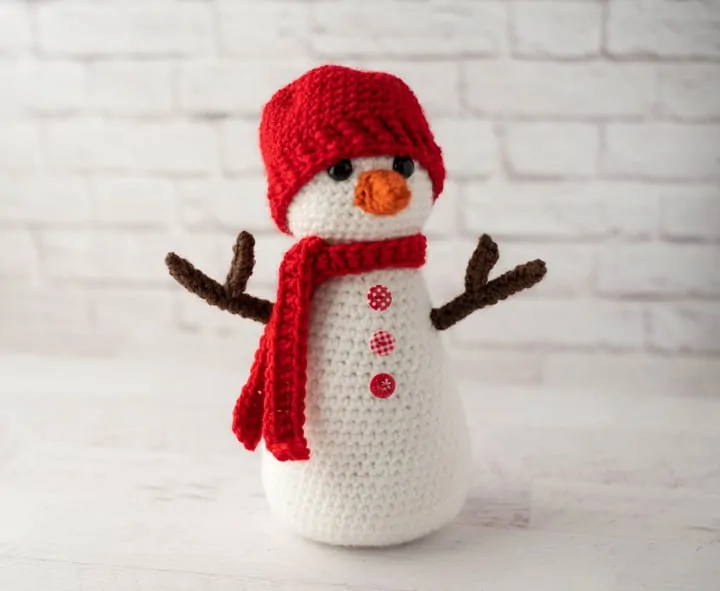 Crochet snowman with red hat and scarf, orange nose and brown twig arms