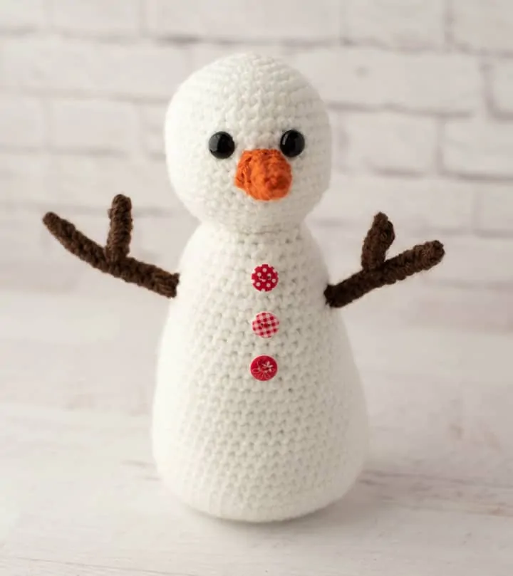 white crochet snowman with brown arms and orange nose