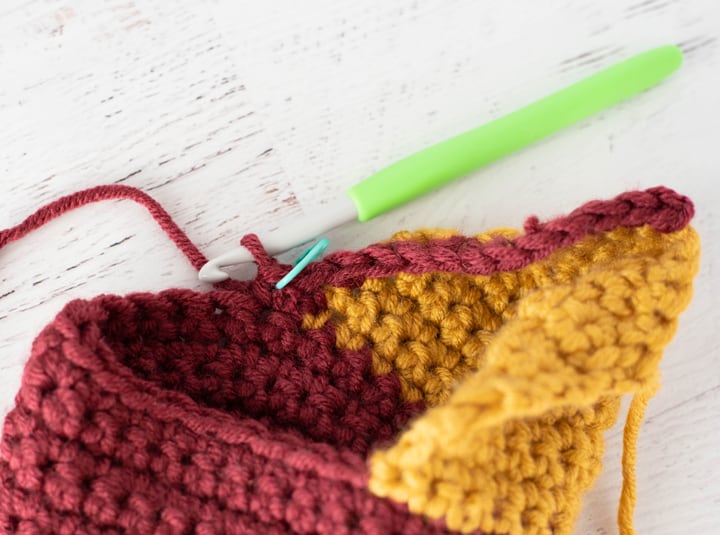 burgundy and yellow crochet stocking heel in progress with green crochet hook