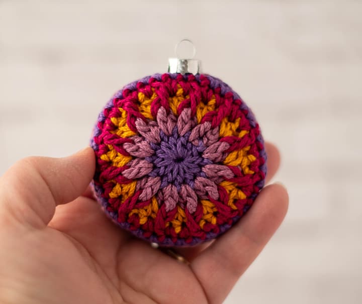 crochet ornament in jewel tone purple, pink and gold yarn.