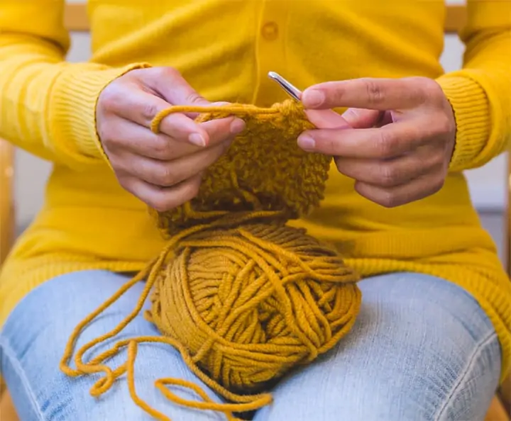 Woman in yellow sweater crocheting with yellow yarn