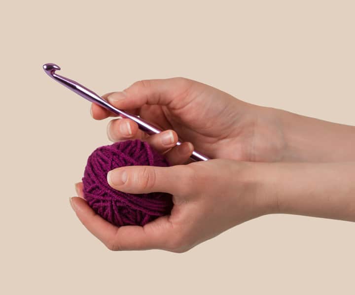 Hands holding pink crochet hook and dark pink yarn
