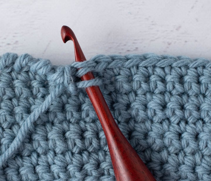 blue crochet piece and wood crochet hook, demonstrating reverse single crochet stitch