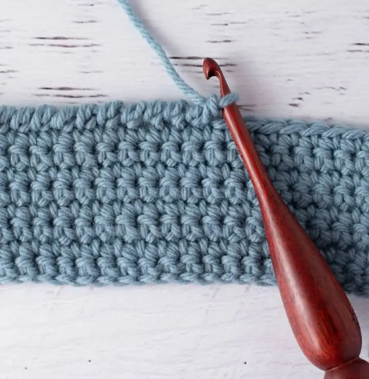 blue crochet piece and wood crochet hook, demonstrating reverse single crochet stitch