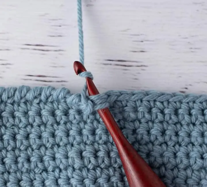 blue crochet piece and wood crochet hook, demonstrating reverse single crochet stitch