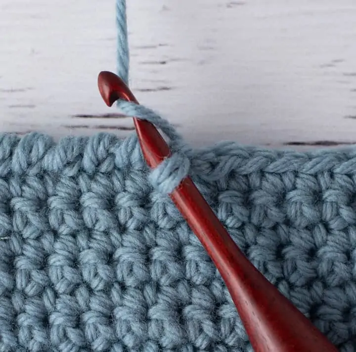 blue crochet piece and wood crochet hook, demonstrating reverse single crochet stitch