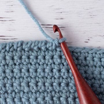 blue crochet piece and wood crochet hook, demonstrating reverse single crochet stitch